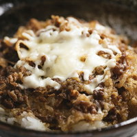 溶けたチーズがたっぷりかかった黒い丼の牛丼の写真