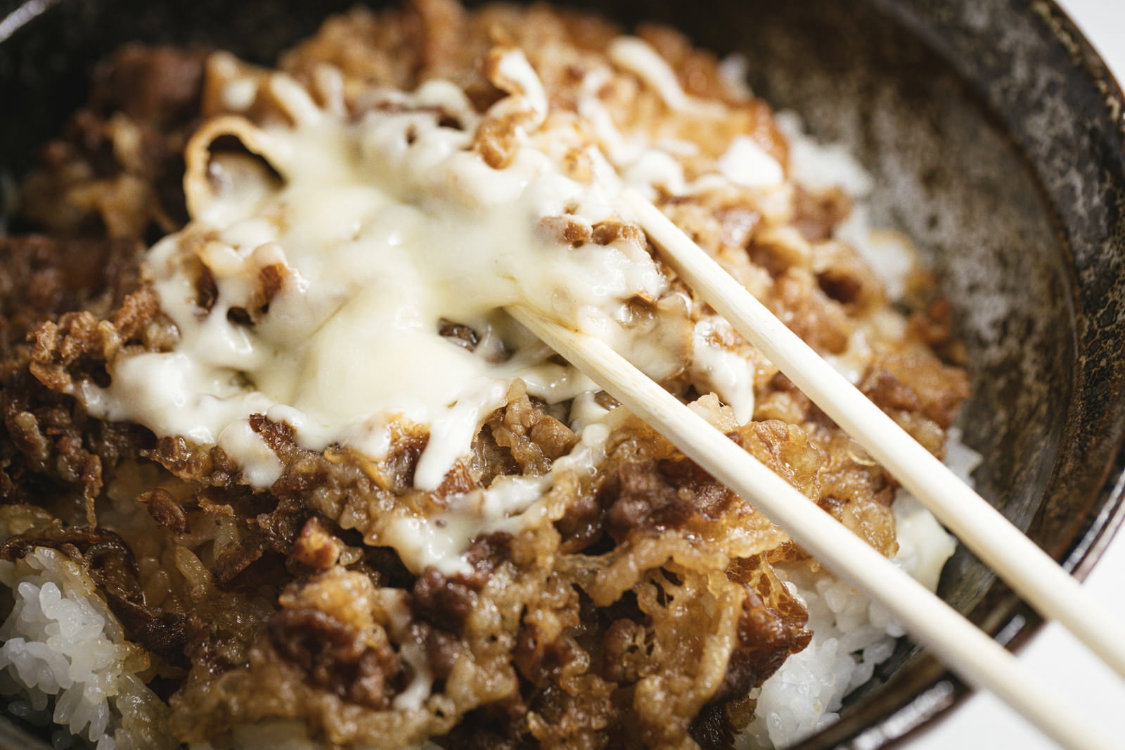 チーズがとろけた牛丼を箸で食べようとしている様子