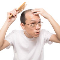 頭皮ケアブラシでマッサージする薄毛男性の写真