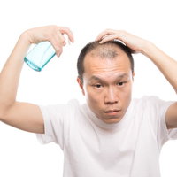 トニックスプレーを頭皮に噴射する薄毛男性の写真
