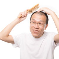 「髪の毛よ生えておいで！」と育毛ブラシでトントンする薄毛男性の写真