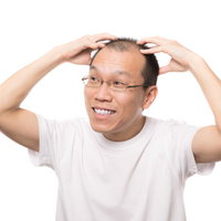 笑顔で頭皮マッサージする男性が鏡で薄毛を確認の写真