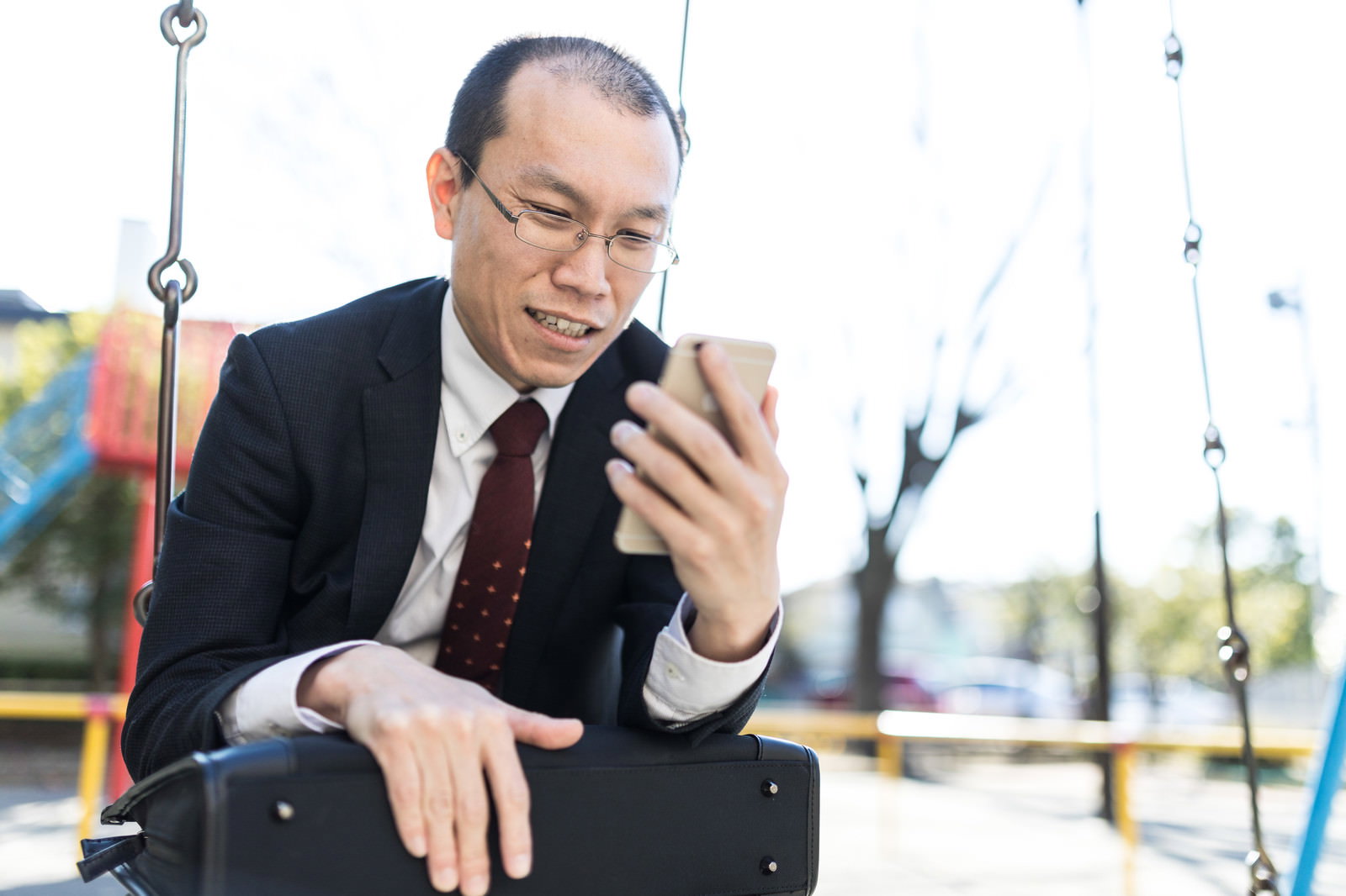 スマートフォンを見て苦笑いする薄毛のスーツ姿の男性［モデル：サンライズ鈴木］