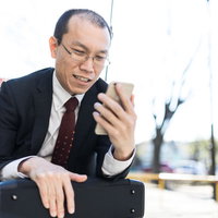 スマートフォンを見て苦笑いする薄毛のビジネスマンの写真