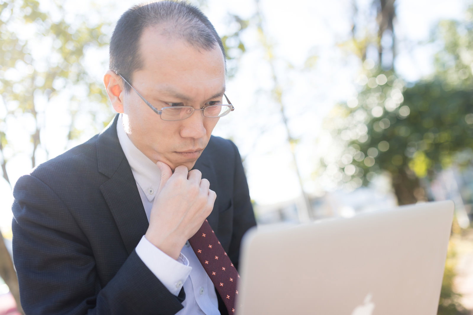 書類を手に持ち悩む表情を見せるスーツ姿の薄毛の男性［モデル：サンライズ鈴木］
