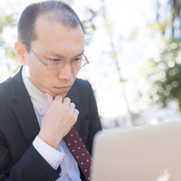 コードとにらめっこする外部委託のエンジニア、スーツ姿で悩む薄毛の男性の写真