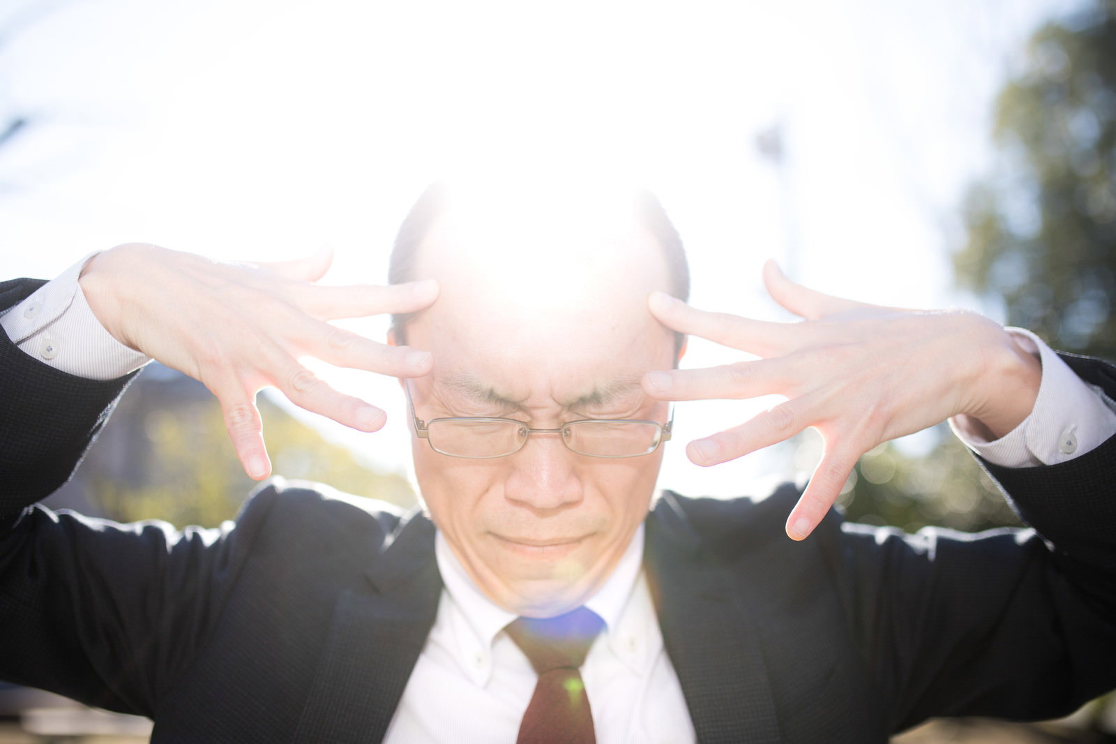 両手で頭を挟み強い光が頭部で反射して眩しく光る、メガネをかけた男性［モデル：サンライズ鈴木］