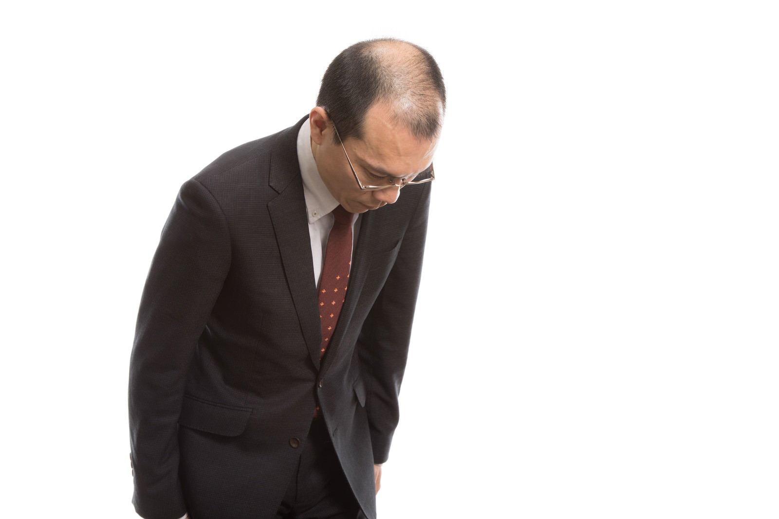 薄毛を気にして浅いお辞儀をする黒いスーツの会社員男性［モデル：サンライズ鈴木］
