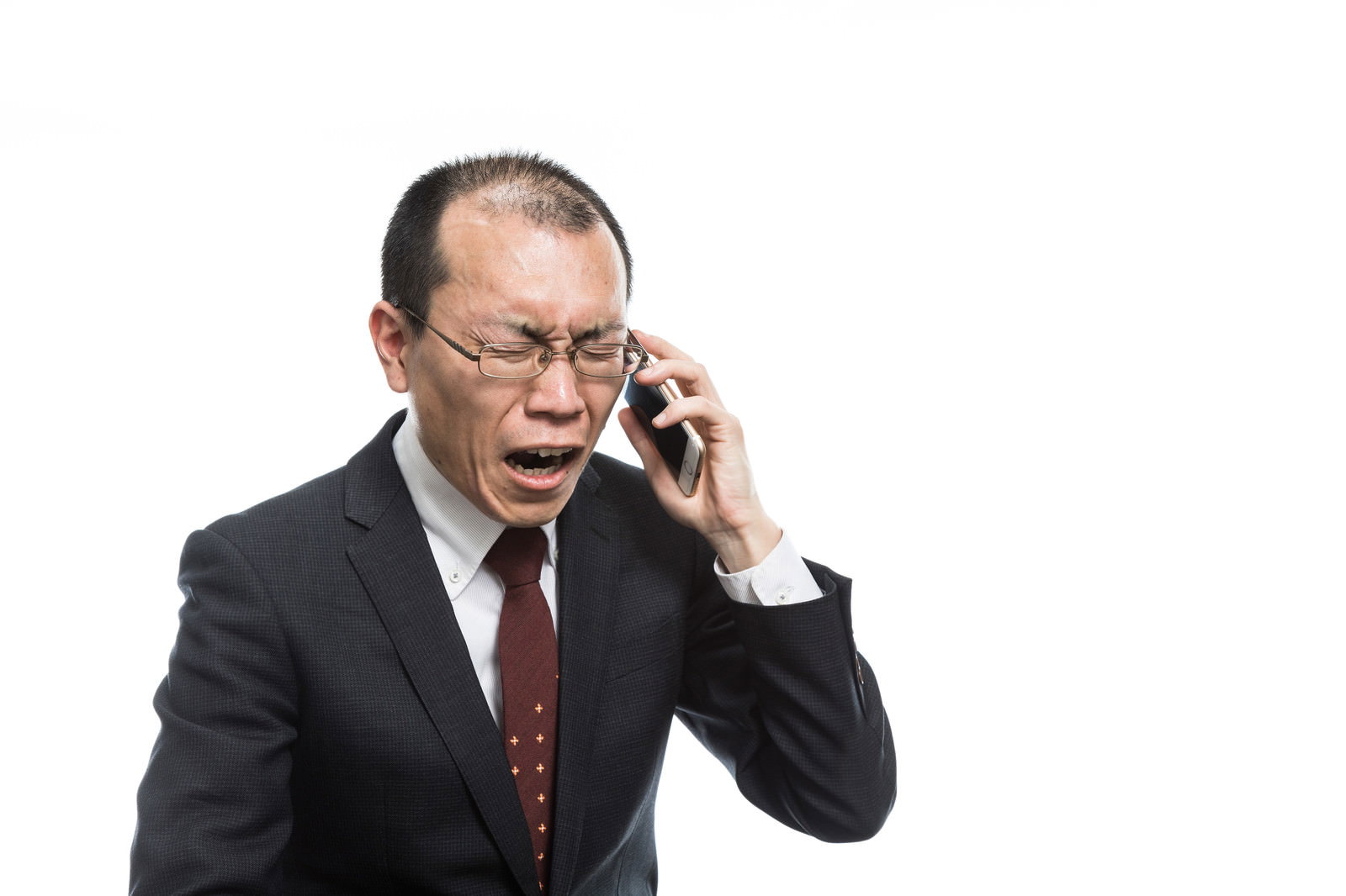 困惑した表情で携帯電話で話すスーツ姿の眼鏡をかけた男性［モデル：サンライズ鈴木］