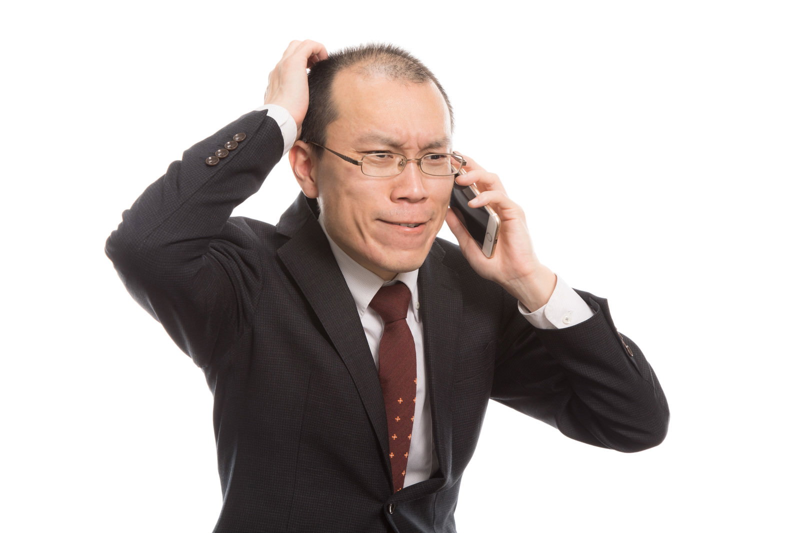 頭を抱えながら電話で話すスーツ姿の眼鏡をかけた男性［モデル：サンライズ鈴木］