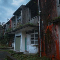 朽ちた外壁と錆びた階段が残る廃アパートの窓の写真