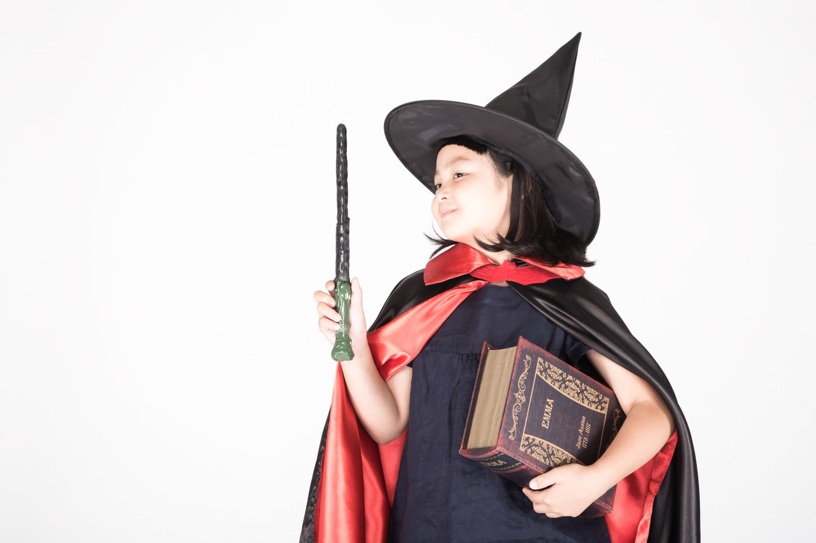 魔法書を持ち黒い三角帽と赤いマントを着た魔女の仮装をした少女［モデル：ゆうき］