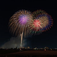 河川敷から打ち上がる色とりどりの花火の写真