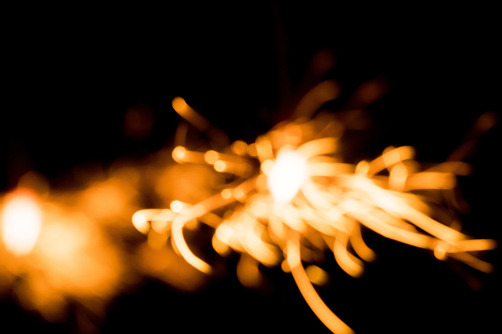 黒い背景にオレンジ色の光が飛び散る線香花火の瞬間