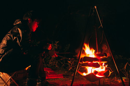 深夜のソロキャンで燃える焚き火と男性のキャンプ風景
