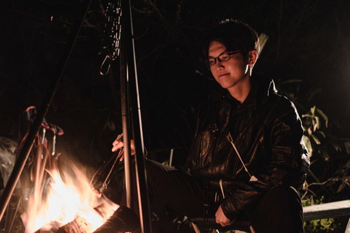 焚き火を前にソロキャンする眼鏡をかけた男性