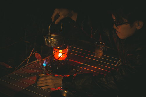 シングルバーナーでやかんのお湯を温める男性