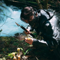 暗い森で刃物を持ち山菜を刈り取る山賊の男性の写真