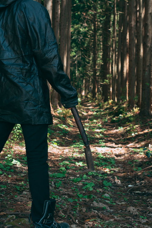 森の木立で黒い鎌を持つ作業着姿の男性