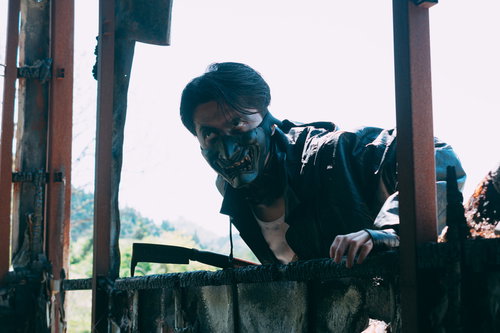 薄暗い廃屋を覗き込む野盗の男性が身を潜めて外をうかがう