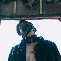 廃墟の窓枠から上を向く黒いジャケット姿の男性の不審な表情の写真