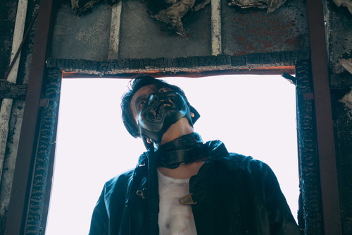 廃墟の窓枠から上を向く黒いジャケット姿の男性の不審な表情