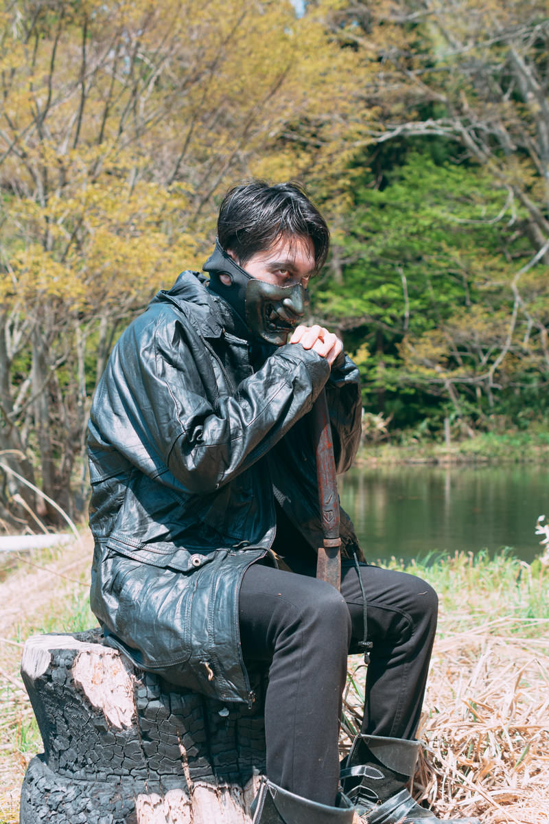山奥で黒い服装の男性が岩に座り獲物を狙う野盗の様子［モデル：花和瞭］