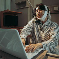 ひげそり失敗で病院入院、頭部包帯姿でノートパソコンを操作する男性の写真