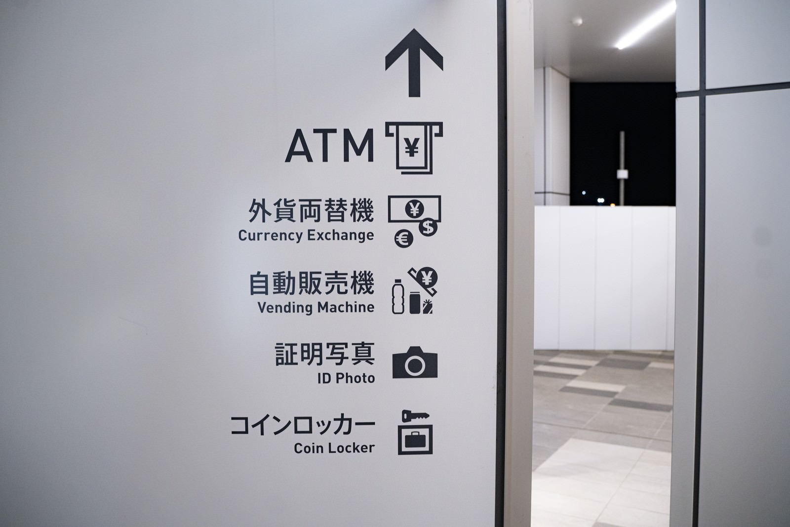 白い壁に設置された施設案内板、上向き矢印とATM・コインロッカーなどの案内表示