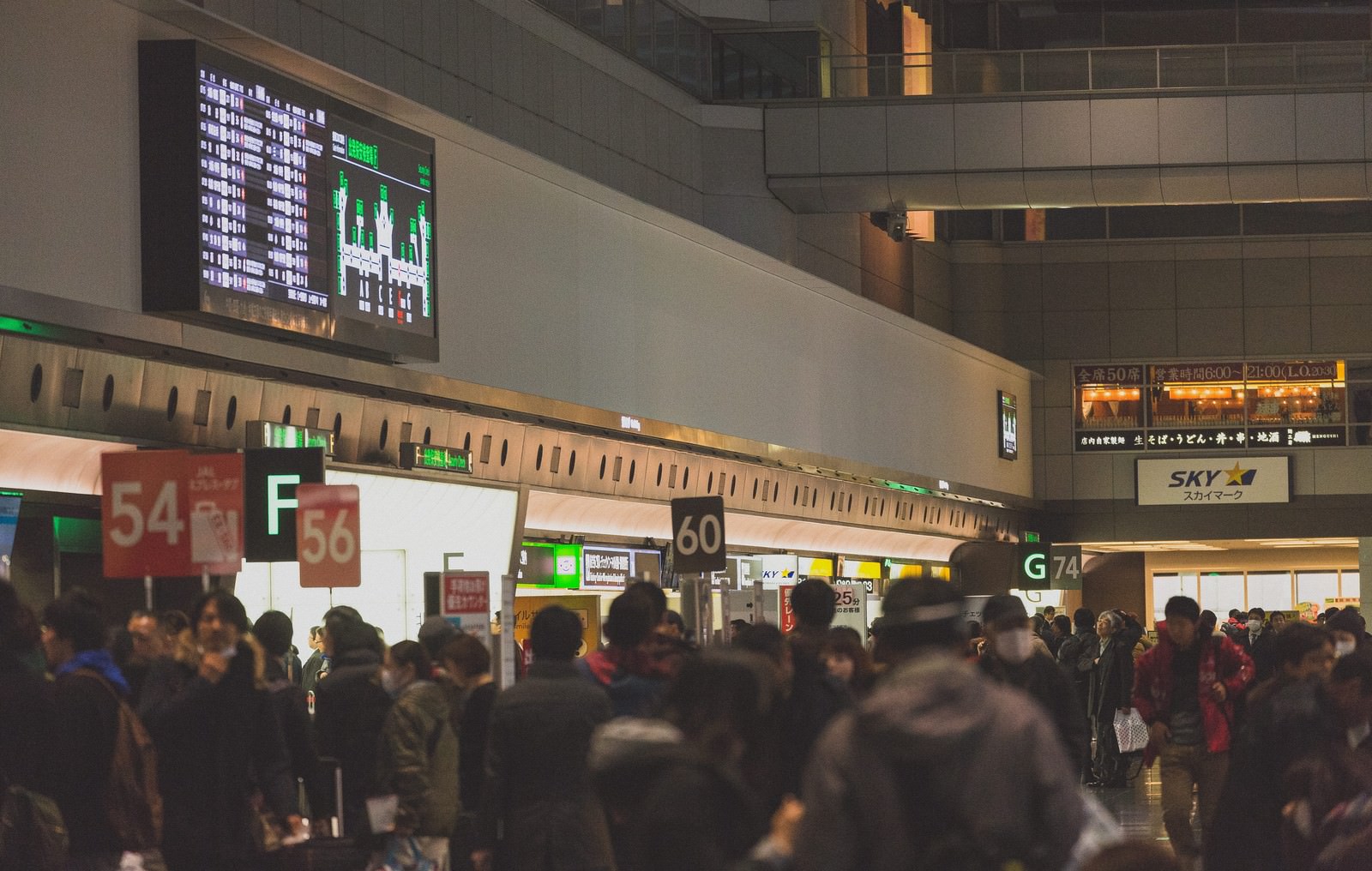 羽田空港のロビーに集まった大勢の乗客と緑色の電子案内板