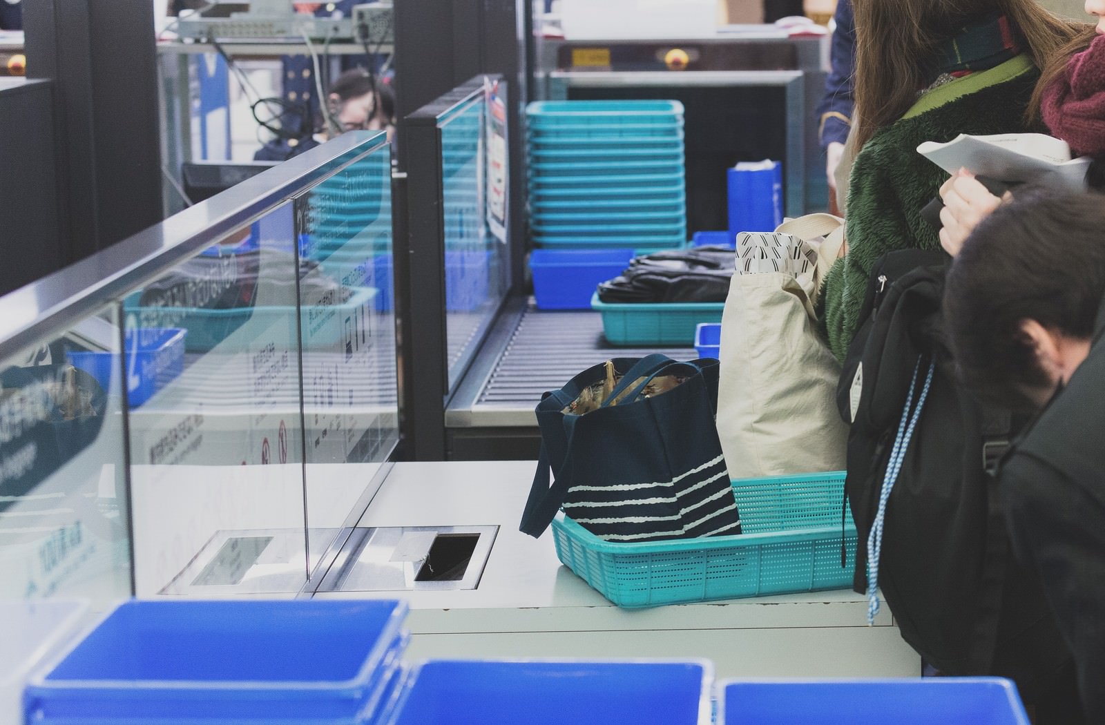 空港の手荷物検査場で青いコンテナの前で荷物を確認する旅行客