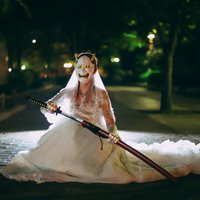般若のお面を付けて刀を抜くウェディングドレス姿の女性の写真