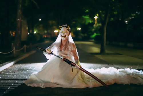 般若のお面を付けて刀を抜くウェディングドレス姿の女性