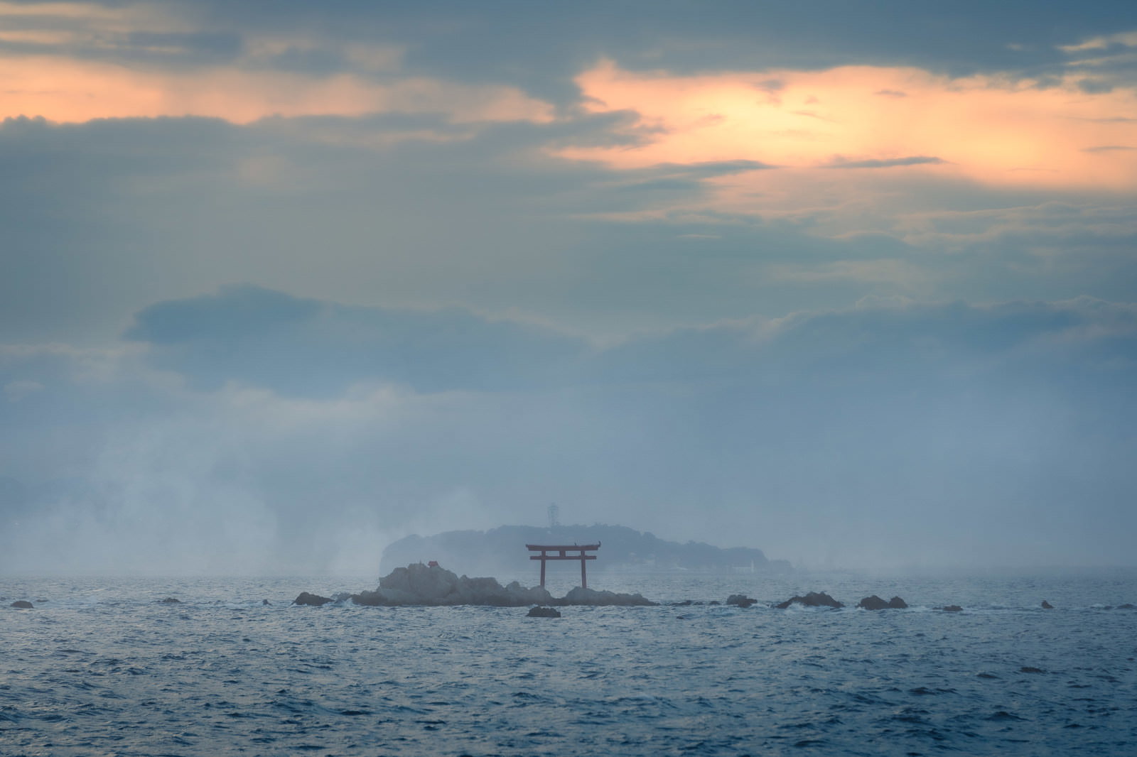 夕焼けに染まった空の下、静かな海に浮かぶ鳥居のシルエット