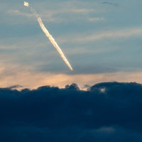 灰色雲が重なるオレンジ色の夕暮れ空に伸びる飛行機雲の写真