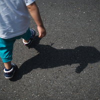 アスファルト道路を散歩する子供の足元と影の写真