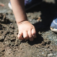 泥を握りしめる子供の手と青い靴での屋外遊びの写真