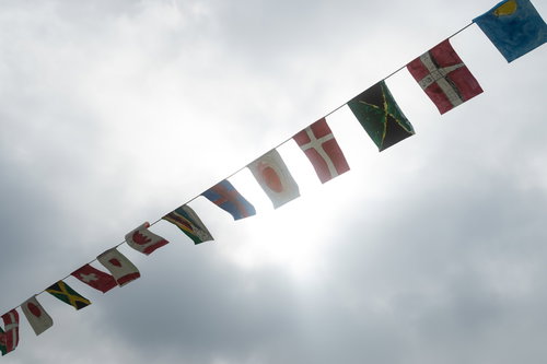 曇り空と風になびくカラフルな万国旗が一列に並ぶ風景