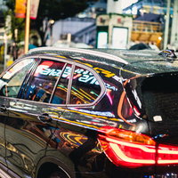 黒塗りの車両に映り込むネオンとブレーキランプの光の写真