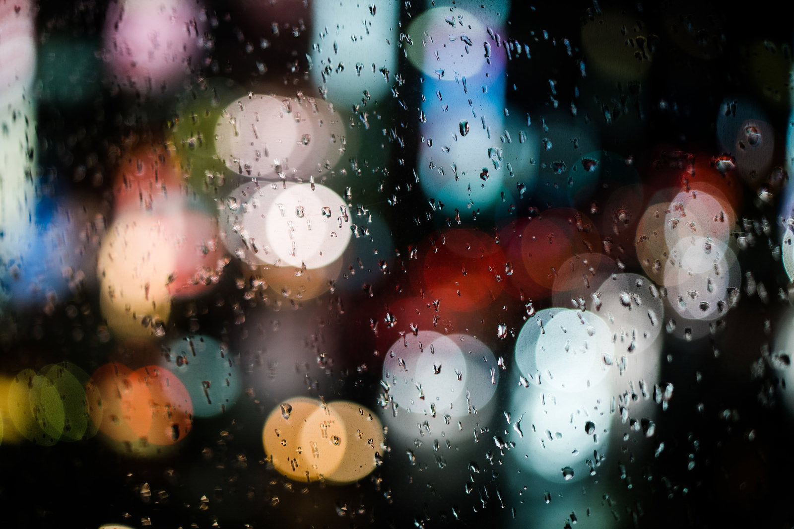 雨に濡れたガラスについた水滴と背景のボケたカラフルな光