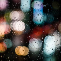 雨粒とネオンの夜景、ボケた光。ガラス面の水滴越しに見る街の光の写真