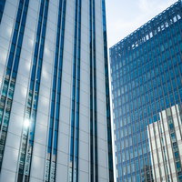 カーテンウォールに反射する複数のビル群と都市風景の写真