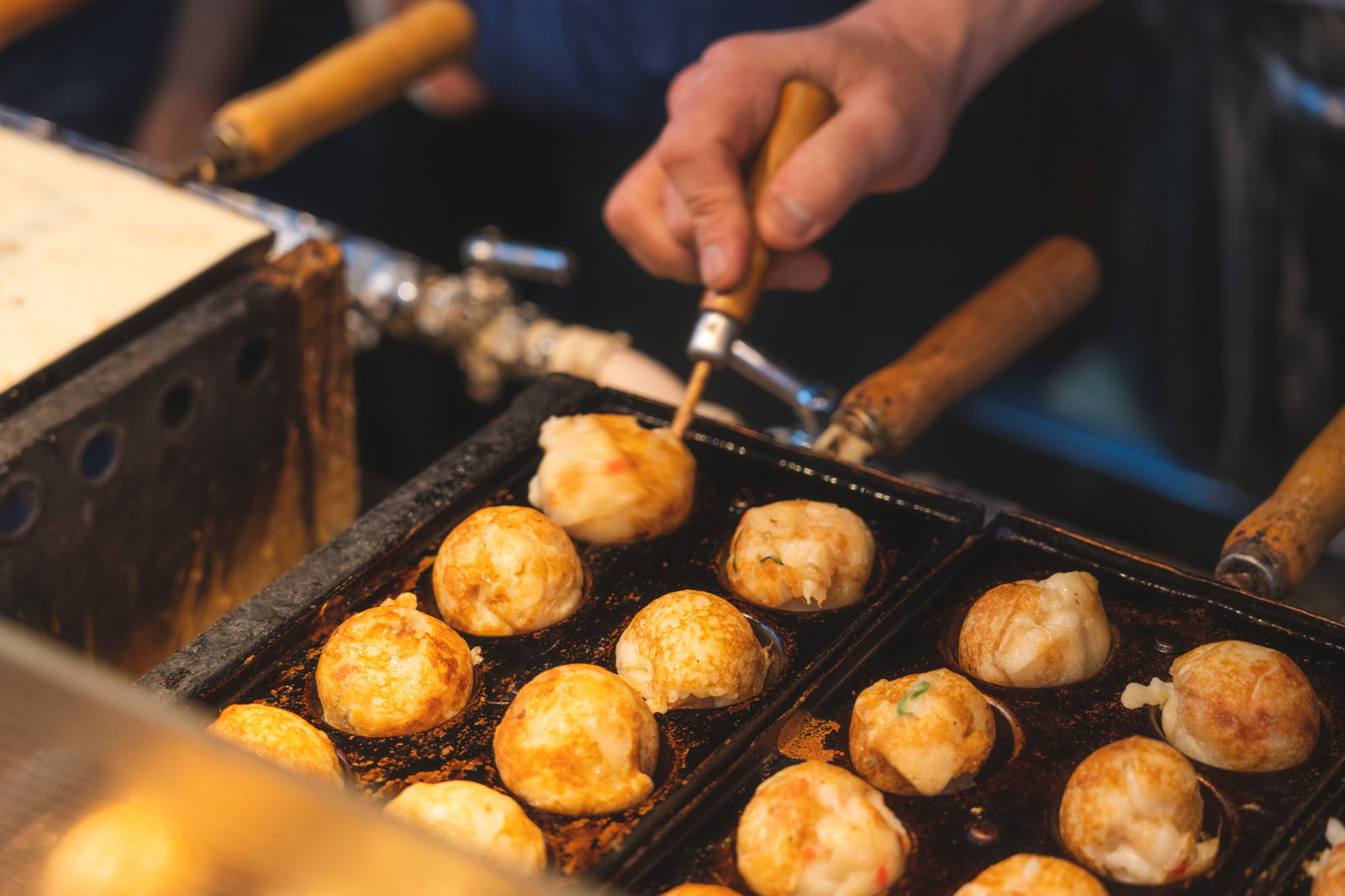 出店で職人が竹串を使ってたこ焼きをひっくり返している調理風景