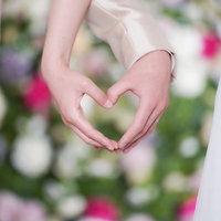 白いウェディングドレスとスーツの新郎新婦が手でハート形をつくるの写真