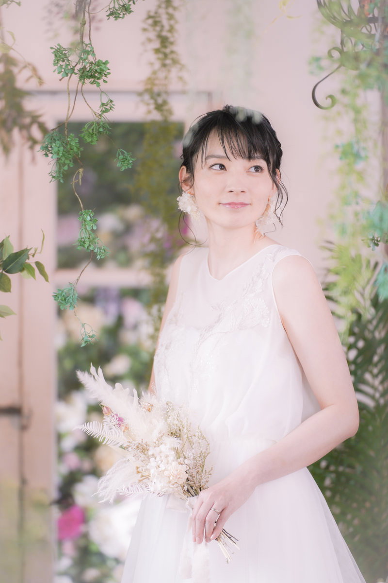 純白のウェディングドレスを着てブーケを持ち微笑む花嫁の女性［モデル：たけべともこ］