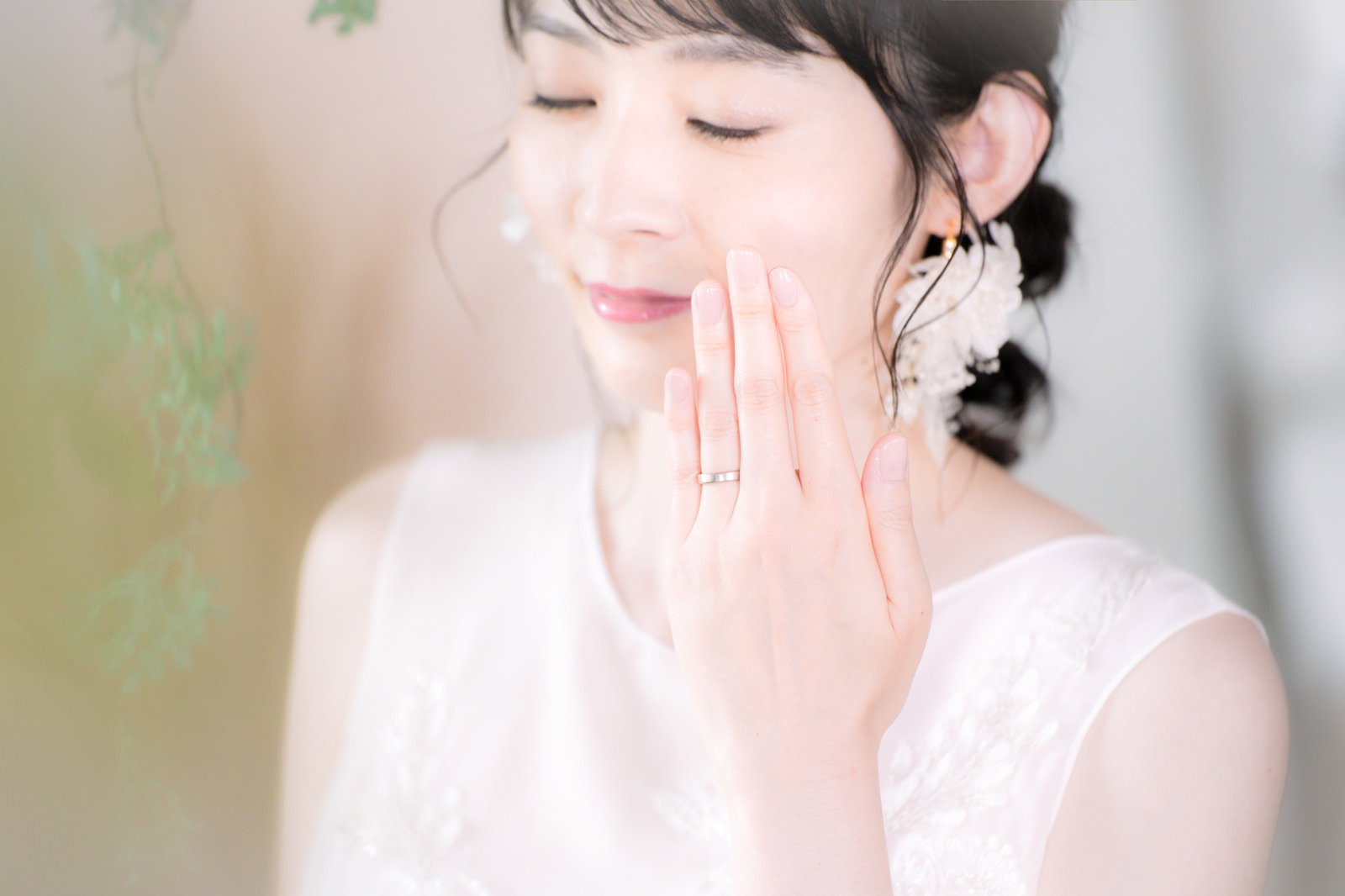 白いドレスを着た女性が左薬指の結婚指輪を見せながら頬に手を添えている［モデル：たけべともこ］