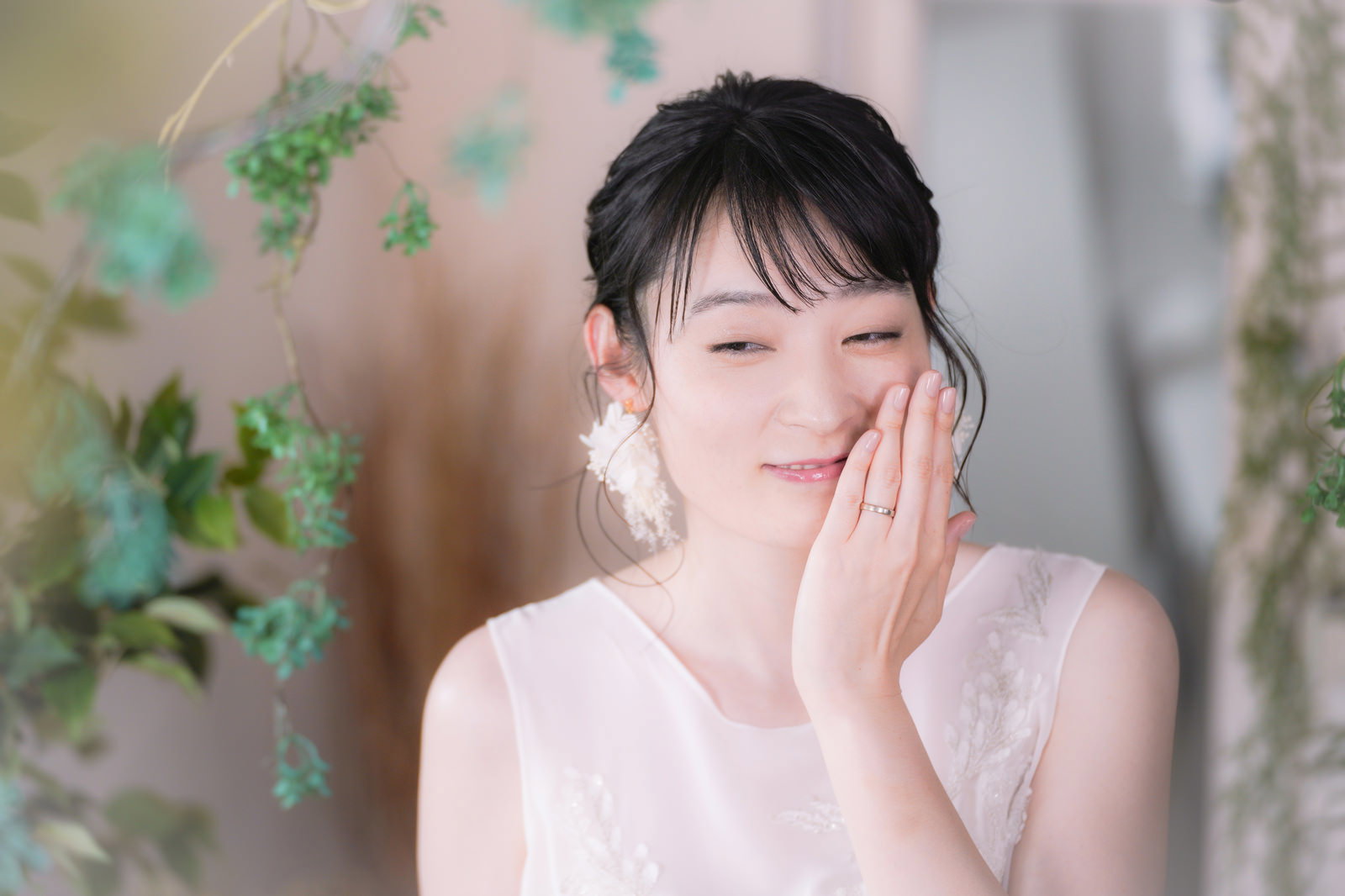 白いウェディングドレスの花嫁が、結婚指輪をした左手を顔の横で見せながら目を閉じて微笑んでいる［モデル：たけべともこ］