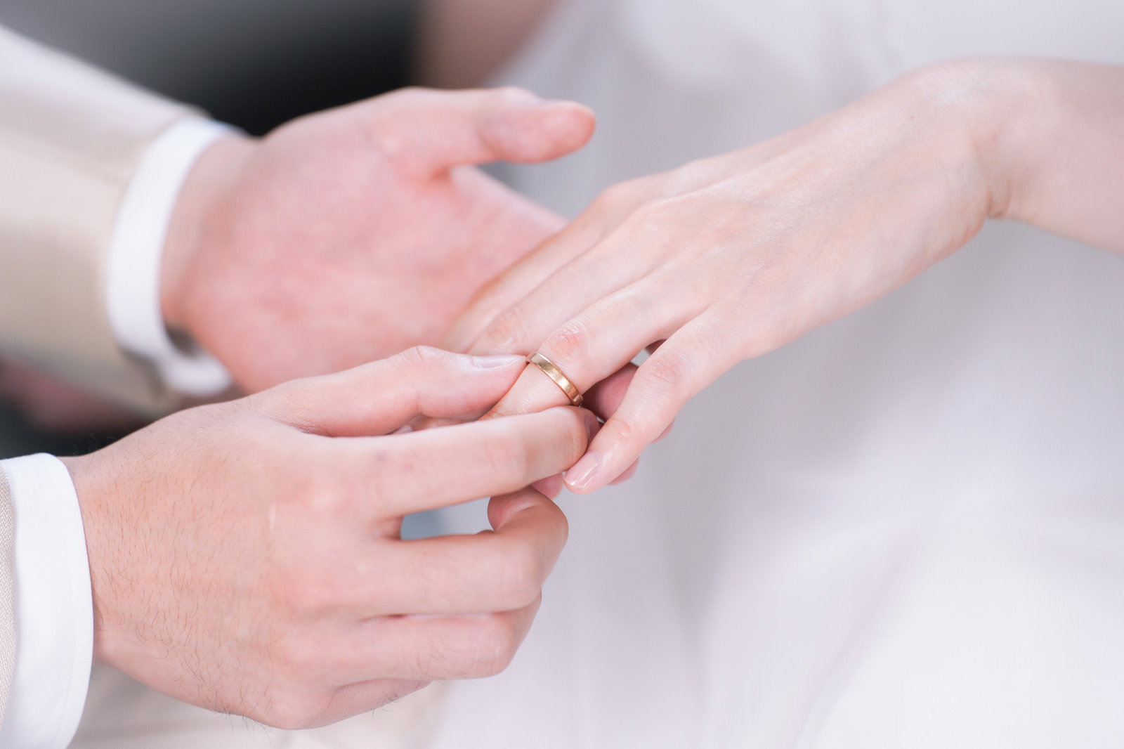 白いウェディングドレスの新婦の左手薬指に結婚指輪をはめる新郎の手［モデル：たけべともこ］