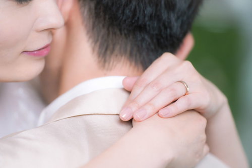 白いドレス姿で彼を抱きしめながら結婚指輪を見つめる女性