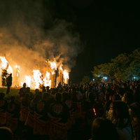 大勢の観客の顔を照らす松明あかしの大きな炎の写真